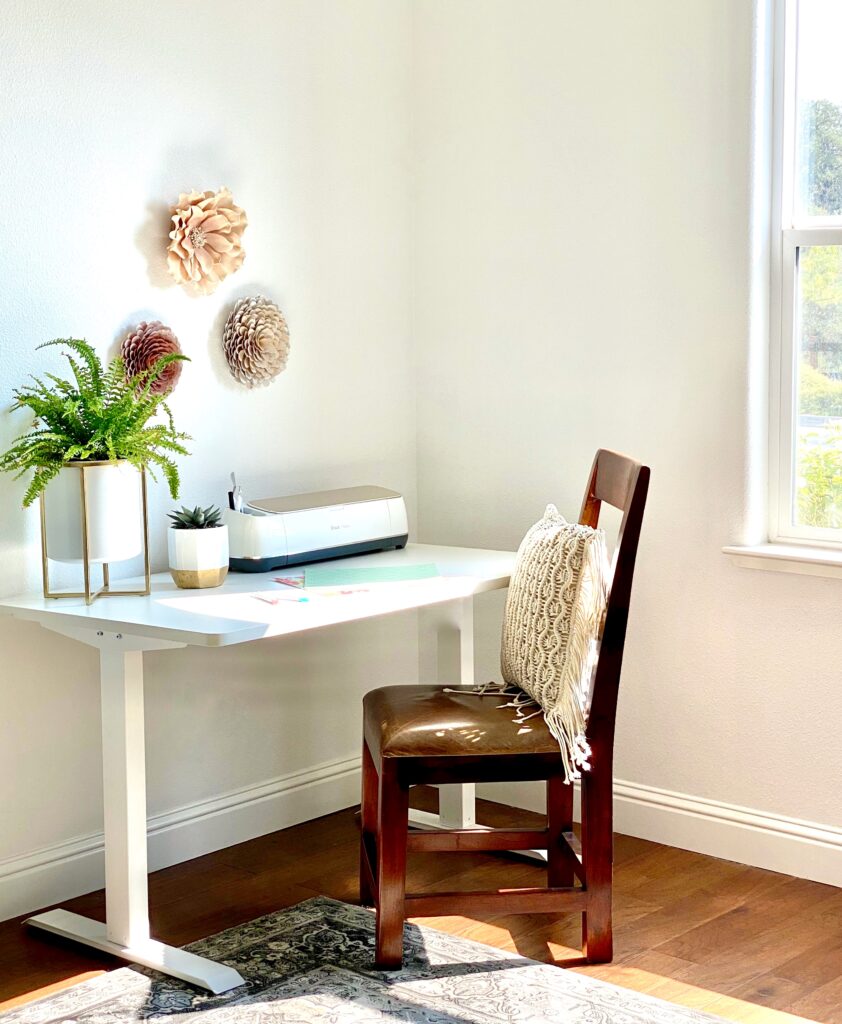 Cricut Maker in a craft room with adjustable craft table a wood chair and a macrame pillow.