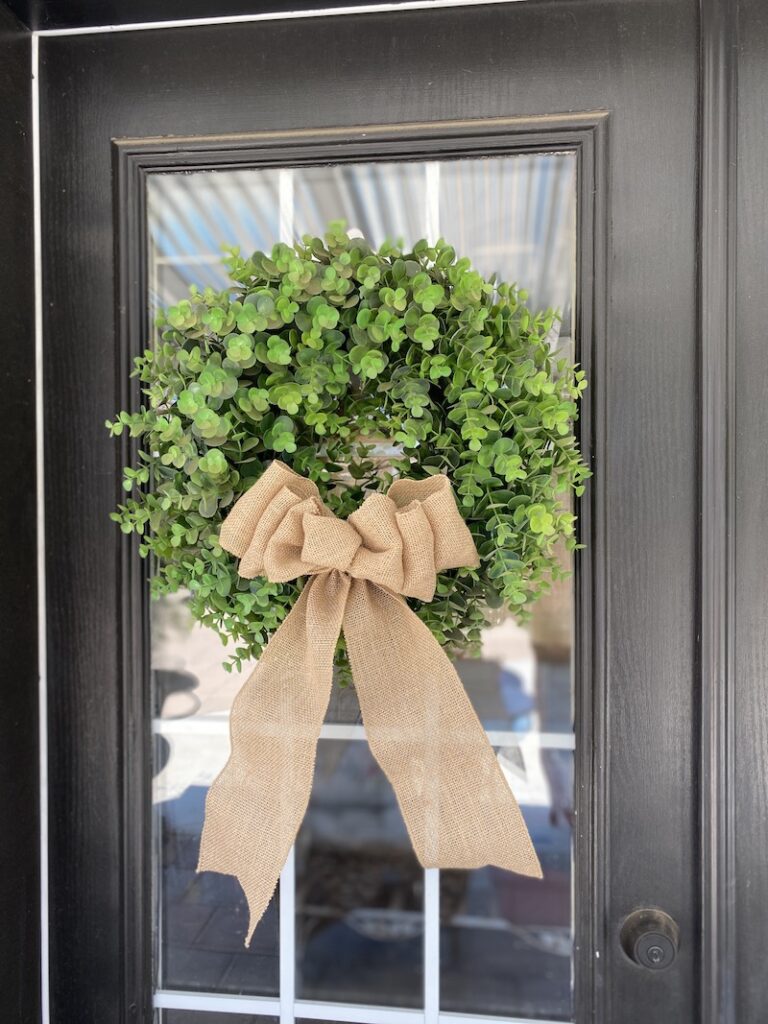 boxwood wreath with a burlap bow hanging on a door
