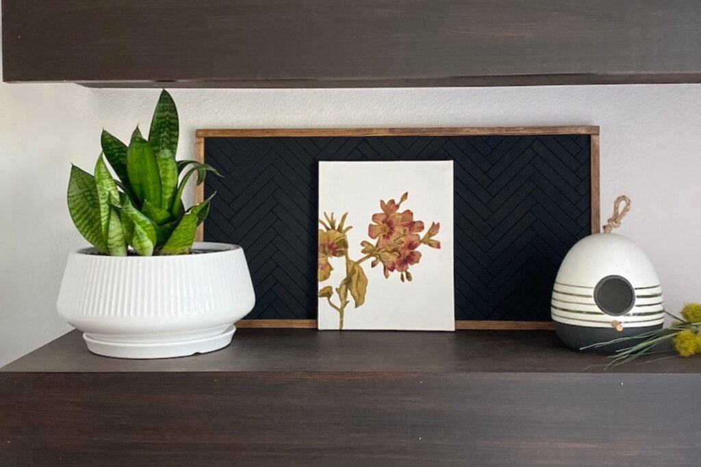 Decoupage Fabric on canvas sitting on a floating shelf with a plant and a ceramic birdhouse